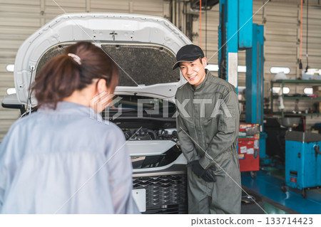 一名男性機械師在修理店向一名女司機解釋汽車 133714423