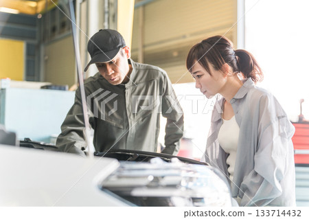 一名機械師在汽車引擎室向一名女顧客解說，一名男性機械師工作人員 133714432