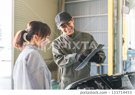 一名機械師在汽車引擎室向一名女顧客解說，一名男性機械師工作人員 133714453