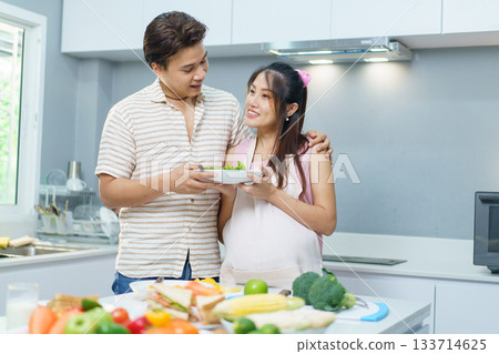 Happy Asian family husband and wife who is currently in pregnancy are preparing or making their food in kitchen together. Then, a man come to embrace his pregnant wife with gently. Happy Asian family husband and wife who is currently in pregnancy are preparing or making their food in kitchen together. Then, a man come to embrace his pregnant wife with gently. 133714625