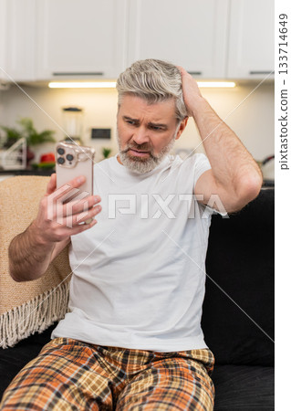 Middle-aged man frowns at smartphone sees failed game and job refusal shakes head no in frustration Middle-aged man frowns at smartphone sees failed game and job refusal shakes head no in frustration 133714649