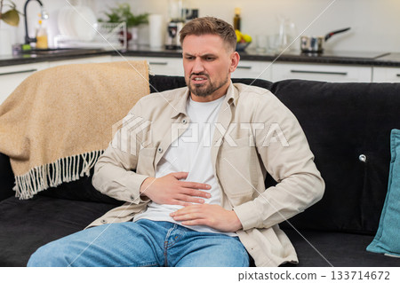 Young man presses hands to stomach cramps pain after heavy fatty food breath control pause routine 133714672