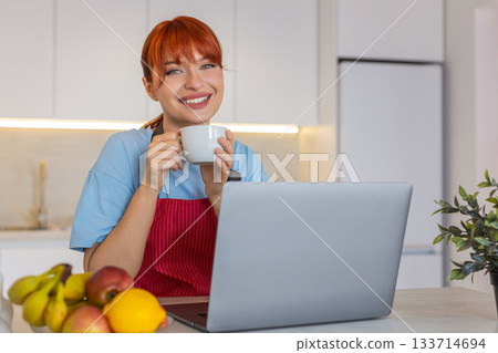 Young woman in kitchen with laptop replies to emails takes coffee sip and manages tasks with focus Young woman in kitchen with laptop replies to emails takes coffee sip and manages tasks with focus 133714694
