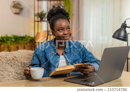 African American young woman reading exciting book with concentration while sitting at table at home African American young woman reading exciting book with concentration while sitting at table at home 133714786