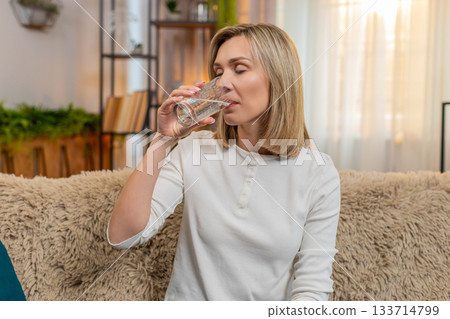 Woman drinking clear filtered water, showing healthy habit and hydration with positive expression Woman drinking clear filtered water, showing healthy habit and hydration with positive expression 133714799