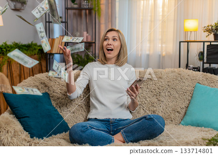 Woman celebrates lottery jackpot with dollar cash falling down while reads win message on smartphone Woman celebrates lottery jackpot with dollar cash falling down while reads win message on smartphone 133714801