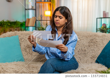Indian woman in stress while looking at unpaid bills on home sofa with frustrated expression Indian woman in stress while looking at unpaid bills on home sofa with frustrated expression 133714831