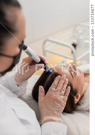 Trichologist doing woman hair regeneration procedure, dermapen microneedling, vitamin injections Trichologist doing woman hair regeneration procedure, dermapen microneedling, vitamin injections 133714877