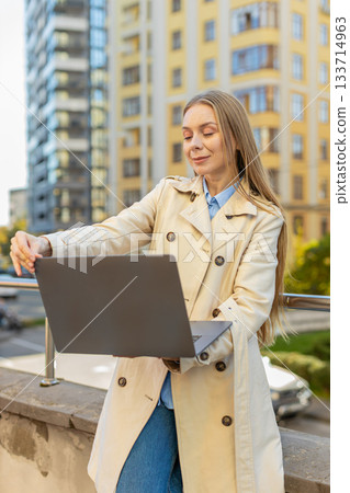 Mature Caucasian businesswoman freelancing remotely, working on laptop netbook in downtown city area 133714963