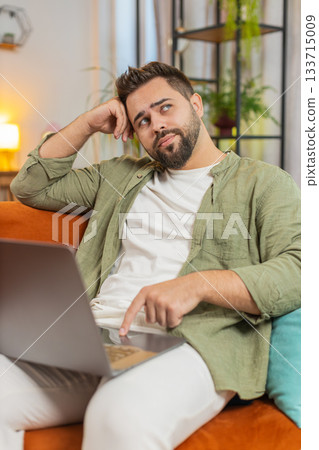 Sleepy young man freelancer with brown hair cannot concentrate on work and types lazily on laptop 133715009