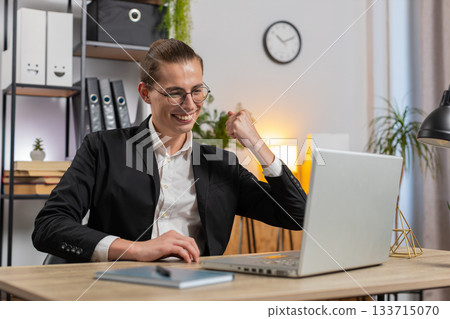 Stylish young Caucasian manager in suit working on laptop netbook shocked by sudden victory at home 133715070