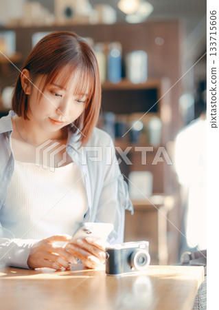 A woman in her 20s relaxing at a cafe with a camera 133715606