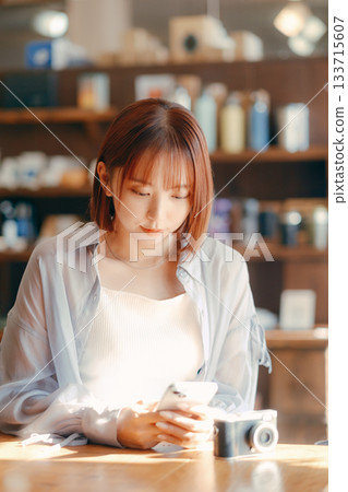 A woman in her 20s relaxing at a cafe with a camera 133715607
