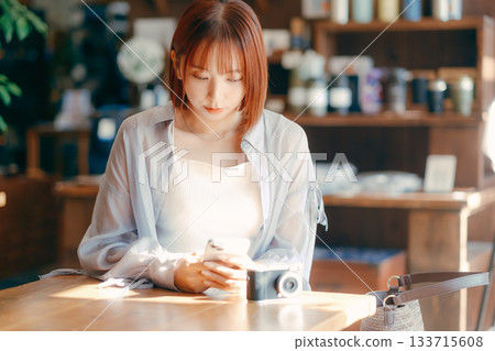 A woman in her 20s relaxing at a cafe with a camera 133715608