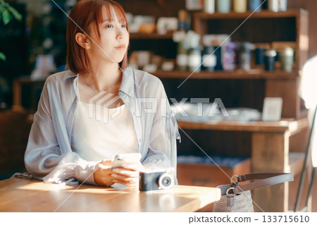 一位二十多歲的女子在咖啡館放鬆，手裡拿著一台相機。 133715610