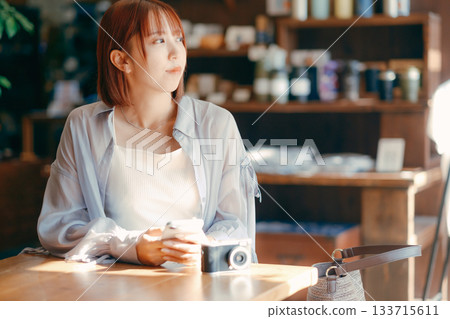 一位二十多歲的女子在咖啡館放鬆,手裡拿著一台相機。 一位二十多歲的女子在咖啡館放鬆,手裡拿著一台相機。 133715611