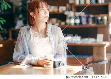 一位二十多歲的女子在咖啡館放鬆,手裡拿著一台相機。 一位二十多歲的女子在咖啡館放鬆,手裡拿著一台相機。 133715612