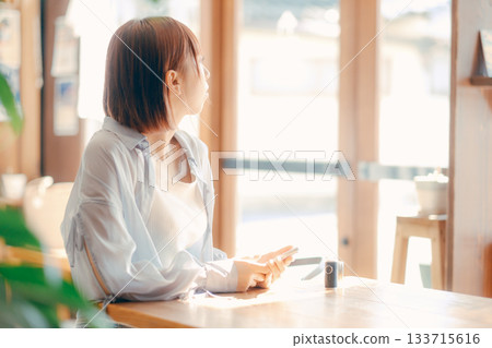A woman in her 20s relaxing at a cafe with a camera 133715616