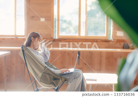 一位二十多歲的女性舒適地坐在椅子上，這是她工作時的場景。 133716036