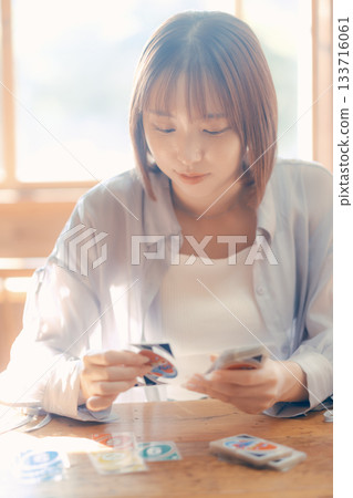 一位二十多歲的女子在陽光明媚的咖啡館裡玩紙牌遊戲。 133716061