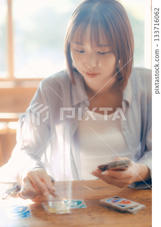 一位二十多歲的女子在陽光明媚的咖啡館裡玩紙牌遊戲。 一位二十多歲的女子在陽光明媚的咖啡館裡玩紙牌遊戲。 133716062