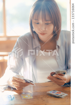一位二十多歲的女子在陽光明媚的咖啡館裡玩紙牌遊戲。 133716064