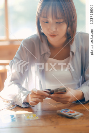 A woman in her twenties enjoying a card game in a sunny cafe 133716065
