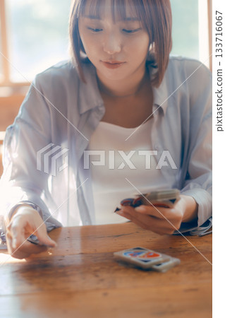 一位二十多歲的女子在陽光明媚的咖啡館裡玩紙牌遊戲。 133716067