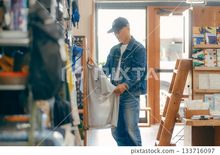 A typical scene of a man in his 60s picking up a magazine in a store A typical scene of a man in his 60s picking up a magazine in a store 133716097
