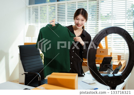 Asian vlogger woman influencer, SME retail store owner smile enjoy selling show live sale online screen smartphone. 133716321