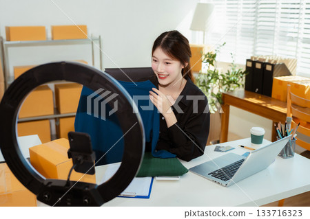 Asian vlogger woman influencer, SME retail store owner smile enjoy selling show live sale online screen smartphone. 133716323