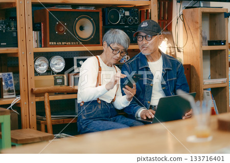 一對老年夫婦在咖啡館使用電腦和智慧型手機進行研究的場景 一對老年夫婦在咖啡館使用電腦和智慧型手機進行研究的場景 133716401