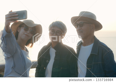 A scene of three parents and children taking a selfie at the beach at dusk A scene of three parents and children taking a selfie at the beach at dusk 133716984