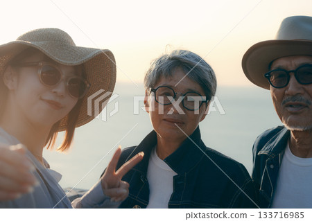 A scene of three parents and children taking a selfie at the beach at dusk A scene of three parents and children taking a selfie at the beach at dusk 133716985