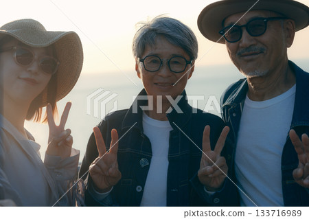 A scene of three parents and children taking a selfie at the beach at dusk 133716989