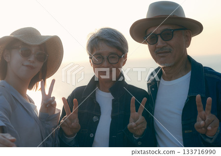 A scene of three parents and children taking a selfie at the beach at dusk A scene of three parents and children taking a selfie at the beach at dusk 133716990
