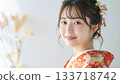 一幅簡潔的日式肖像畫，畫中是一位微笑的年輕女子，身穿紅色和金色振袖和服。 133718742