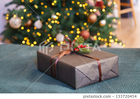 Christmas gift box decorated with ribbon and red berries in front of glowing festive tree lights Christmas gift box decorated with ribbon and red berries in front of glowing festive tree lights 133720454
