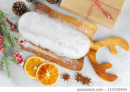Traditional Christmas Stollen, sweet fruit loaf with sugar icing on wooden board and festive decor 133720459