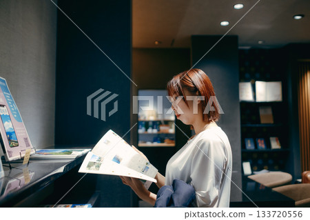 一位二十多歲的女子在飯店大廳看著一份宣傳冊。 一位二十多歲的女子在飯店大廳看著一份宣傳冊。 133720556