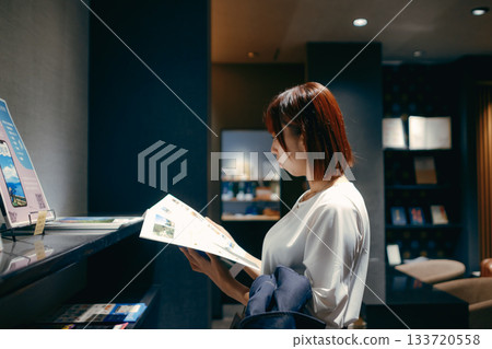A woman in her twenties looking at a pamphlet in a hotel lobby A woman in her twenties looking at a pamphlet in a hotel lobby 133720558