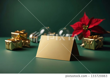 Blank gold folded card surrounded by gold gift boxes, ornaments and poinsettia on green surface. Studio still life mockup. Christmas holiday greeting concept. Design for card, invitation, copy space 133720863