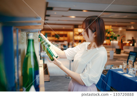 一位二十多歲的女上班族正在飯店紀念品櫃檯挑選當地清酒。 133720888