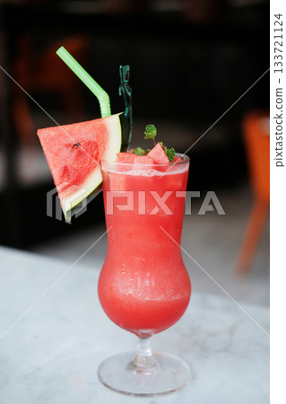 A glass of watermelon smoothie with red star spoon on wooden table in tropical of cafe A glass of watermelon smoothie with red star spoon on wooden table in tropical of cafe 133721124
