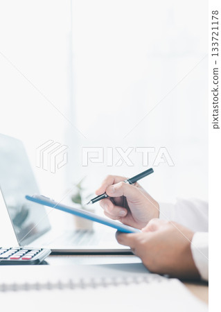 A businesswoman reviews financial report while holding documents and pointing with pen at office desk. Concept of accounting, budget management, financial analysis and corporate business planning. 133721178