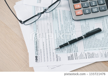 Concept of tax filing and accounting. Close up of US individual income tax return form with pen and calculator on office desk, symbolizing financial planning, budget management and payment accuracy. Concept of tax filing and accounting. Close up of US individual income tax return form with pen and calculator on office desk, symbolizing financial planning, budget management and payment accuracy. 133721476