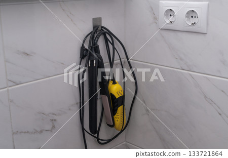 Hair straightener and shoe dryer on tiled bathroom wall. Double socket provides power for these grooming appliances in modern home interior. modern bathroom. Hair straightener and shoe dryer on tiled bathroom wall. Double socket provides power for these grooming appliances in modern home interior. modern bathroom. 133721864