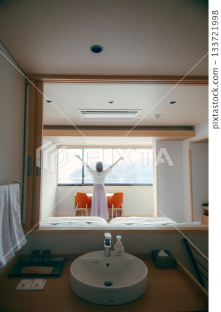 A scene of a woman in her twenties looking at the spectacular view from a hotel room 133721998