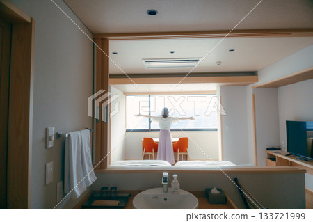 A scene of a woman in her twenties looking at the spectacular view from a hotel room 133721999