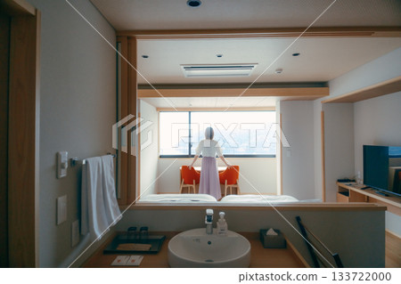 一位二十多歲的女子正從飯店房間欣賞壯麗的景色。 133722000